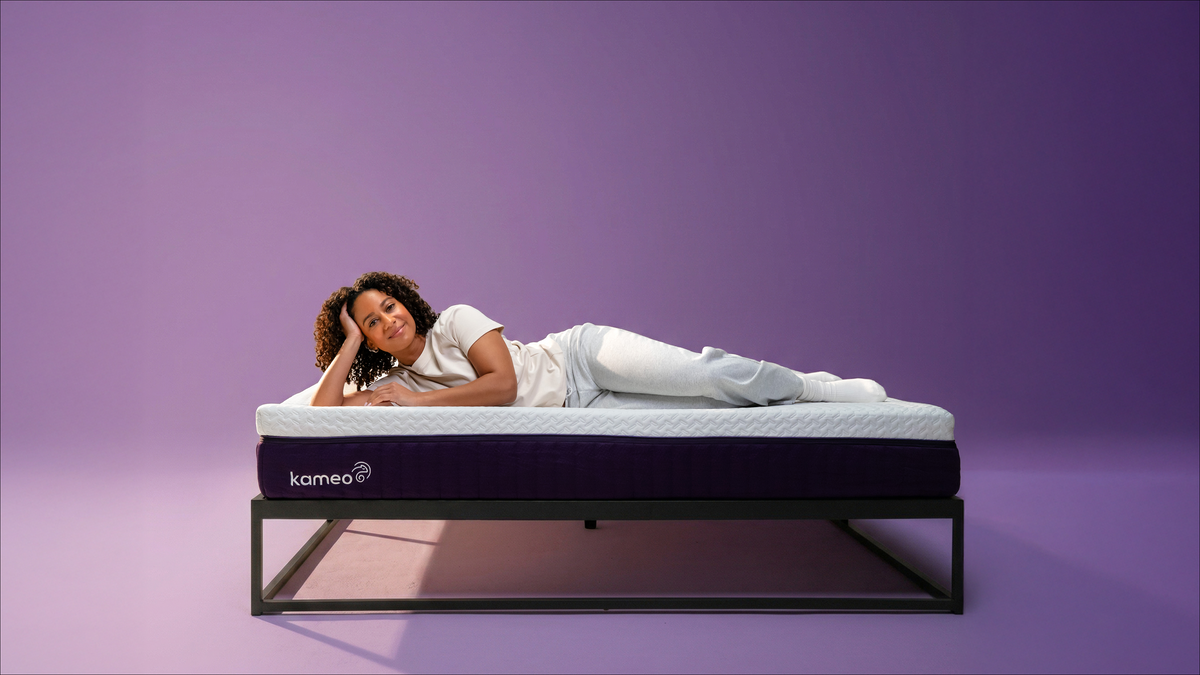 Vrouw ligt ontspannen op het Kameo Flex Matras in de paarse studio-setting
