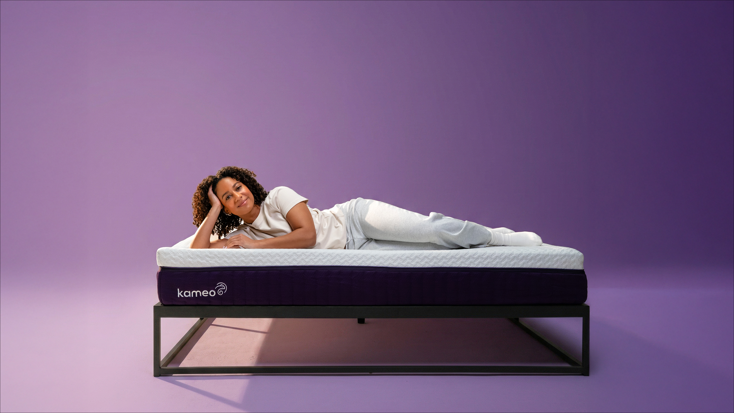 Vrouw ligt ontspannen op het Kameo Flex Matras in de paarse studio-setting